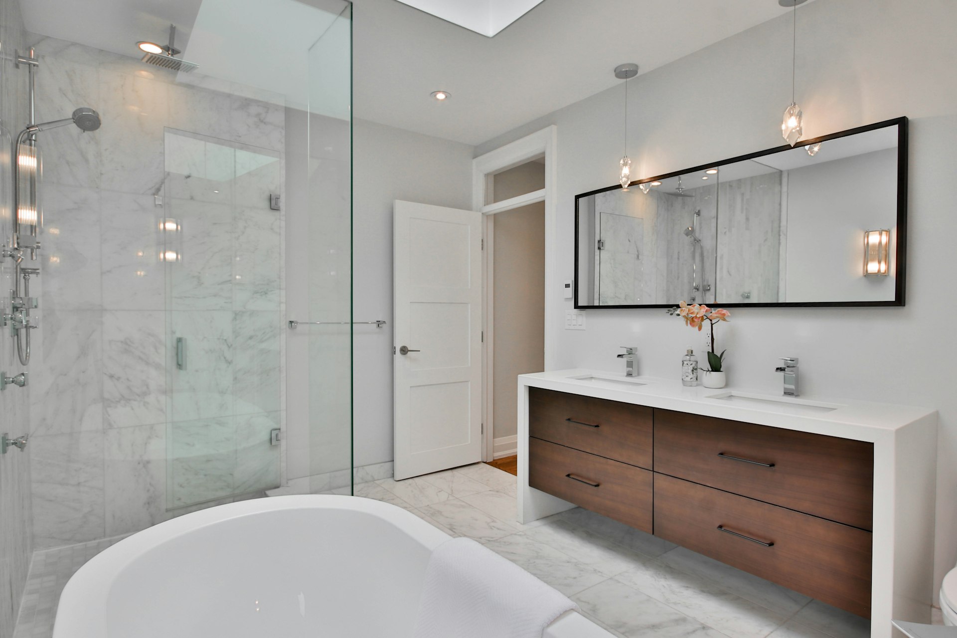 A finished bathroom with a walk-in marble shower, freestanding bath and twin vanity