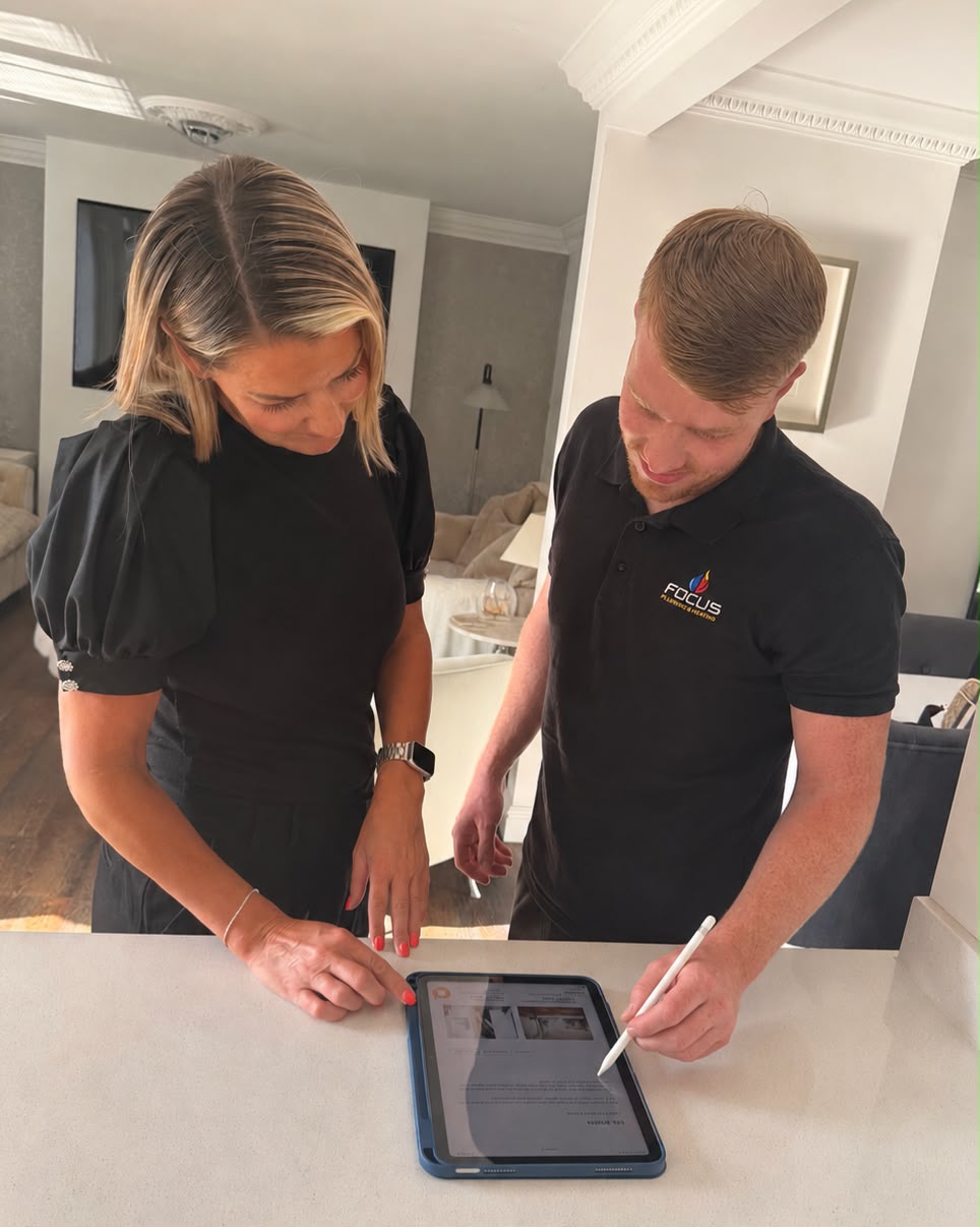 A Focus Plumbing & Heating engineer talking a customer through a quote on a tablet at her kitchen worktop